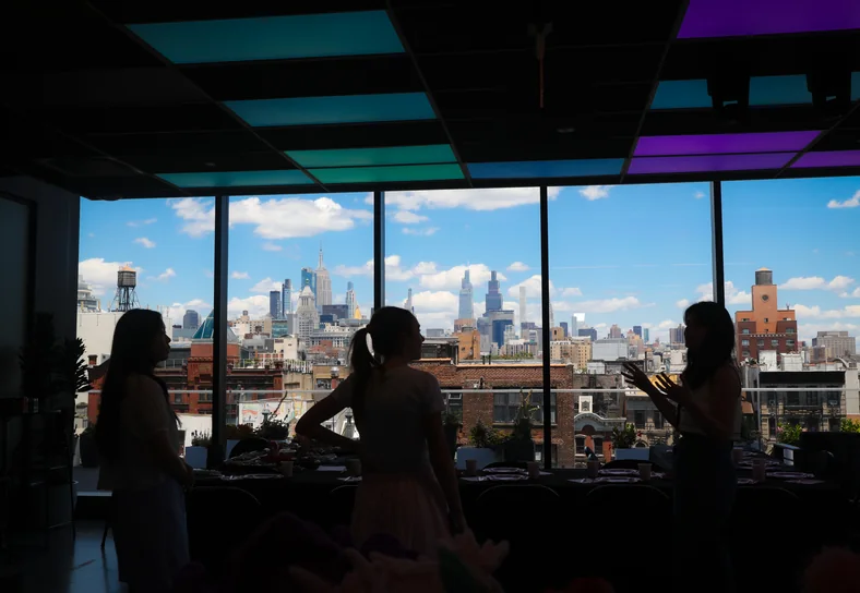 Three women in silhouette against a window wall, the Manhattan skyline behind them