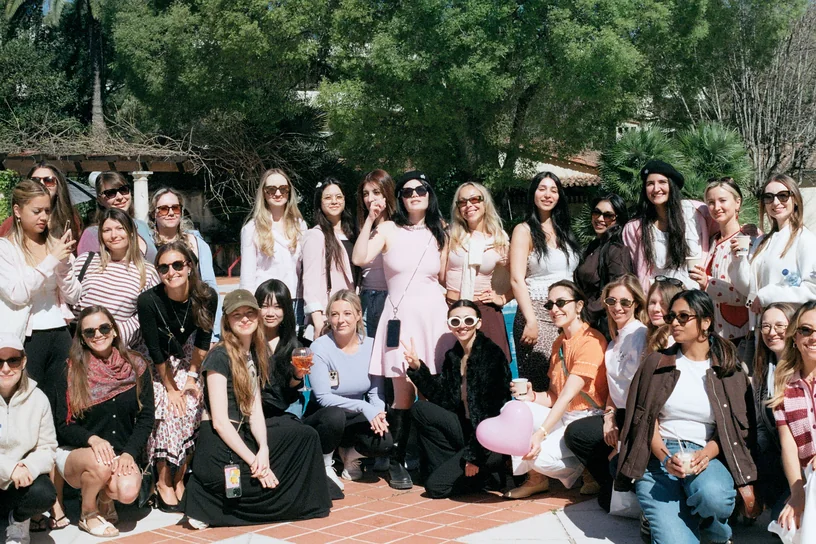 Around thirty women packed together for a group photo on a sunlit terrace among palm trees